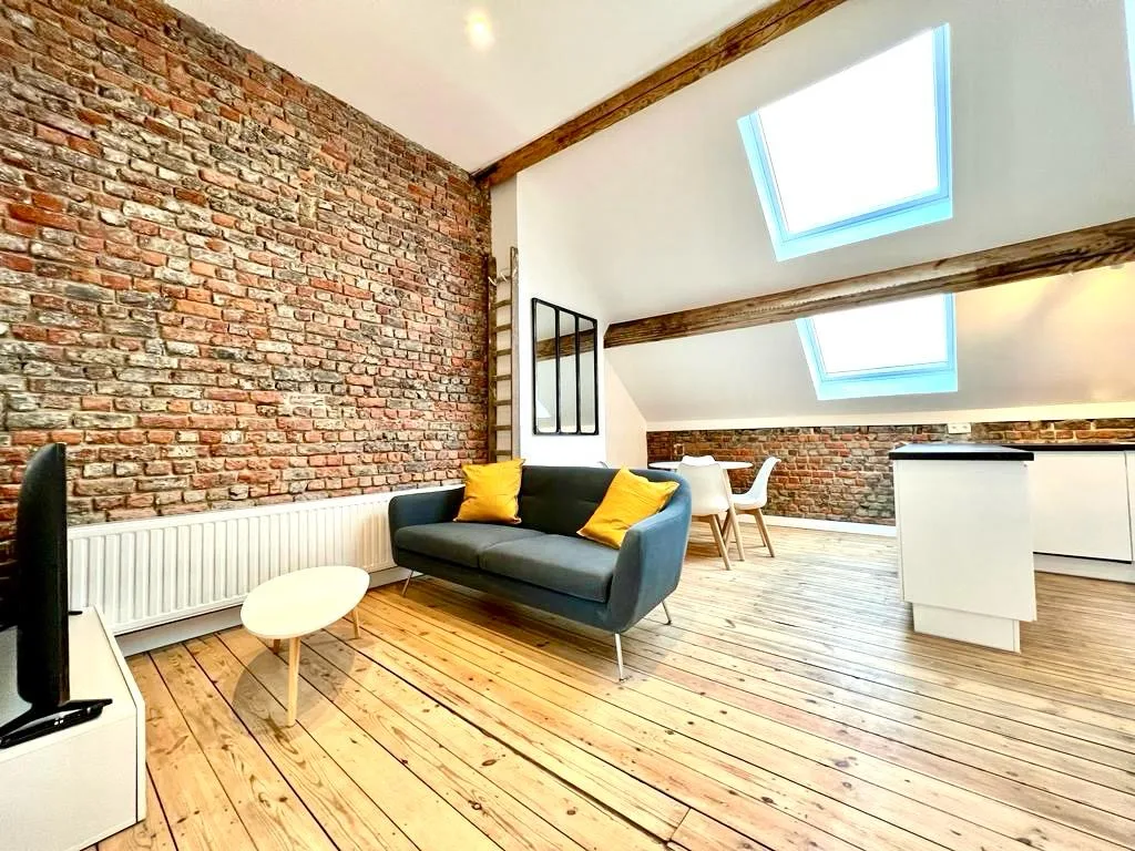 Loft sous combles : mur de briques apparentes conservé, pentes et plafond repeints en blanc, deux velux, plancher en pin